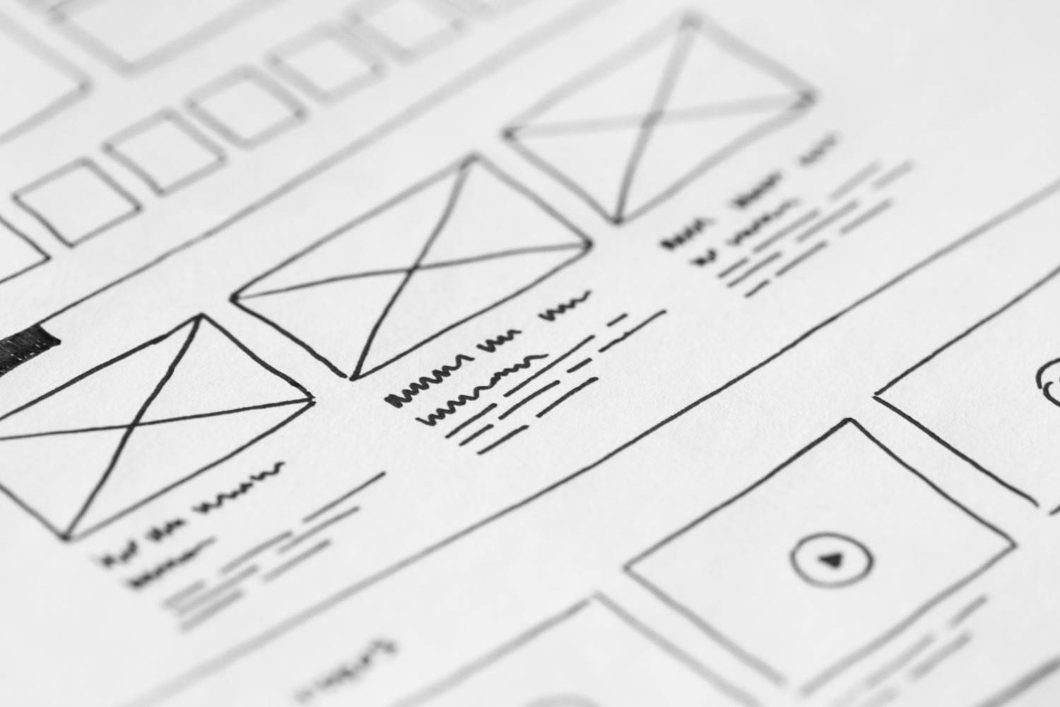 Eine Nahaufnahme eines skizzierten Website-Drahtmodells auf Papier, mit Rechtecken für Bilder oder Banner und Linien, die Text anzeigen. Dieses vorläufige Webdesign-Konzept dient als Vermittlungstool für Ideen und Layoutstrategien.
