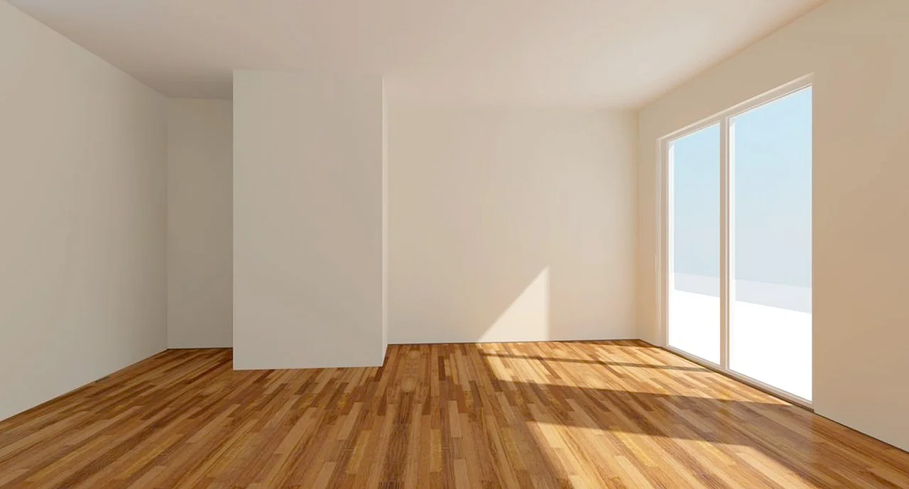 Ein leerer Raum mit Holzboden, weißen Wänden und einem großen Fenster auf der rechten Seite lässt Sonnenlicht herein und schafft eine helle und geräumige Atmosphäre. Dieser einladende Raum wartet auf seine neue Bestimmung durch Vermittlung und bietet endlose Möglichkeiten.