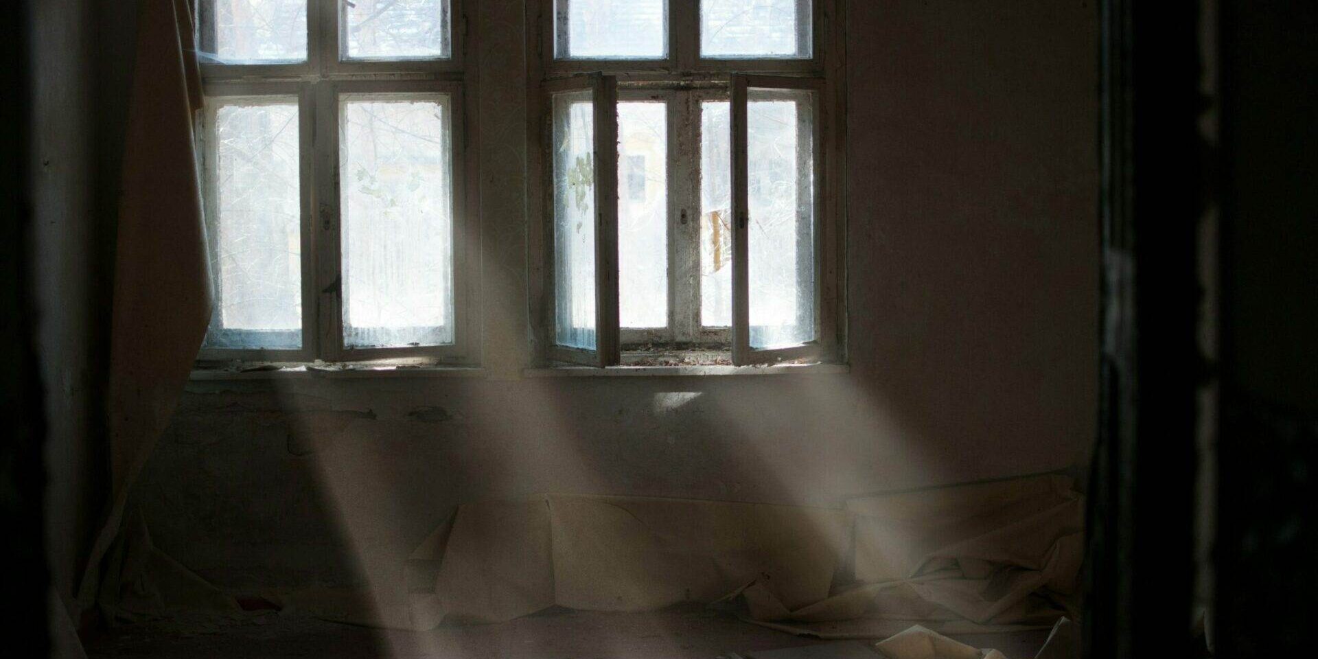 Lichtstrahlen, die durch die Fenster eines leeren Raumes fallen, mit sichtbaren Staubpartikeln.