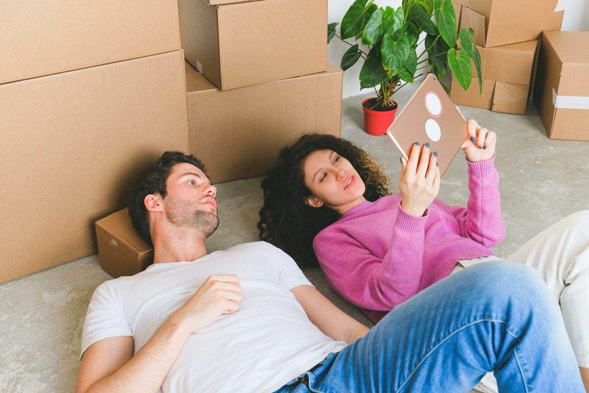 Junges Paar bei der Wohnungssuche in Wien, sitzt zwischen Umzugskartons und recherchiert Mietwohnungen in Wien auf einem Tablet – ideal für Wohnungssuche-Tipps und Budgetplanung für günstige Mietwohnungen in Wien.